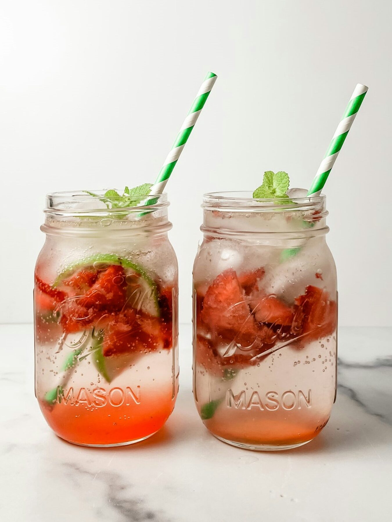 Two mason jar mocktails with strawberry, lime and mint