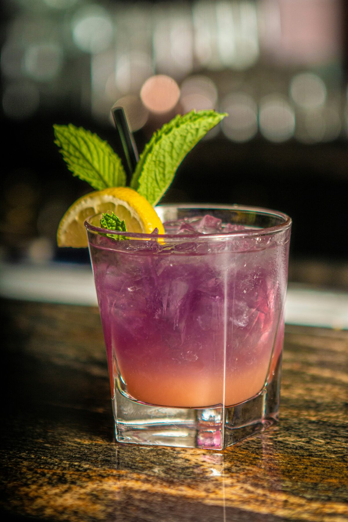 Purple mocktail with mint and lemon garnish on a bar counter